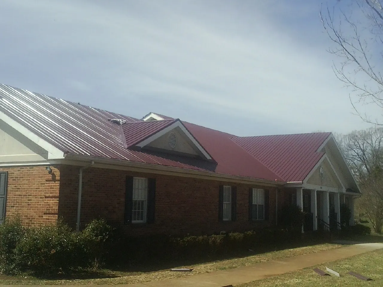 Red metal roof with gabled entries on a long brick building, from a Hail Damage Roof Repair job in Elderton