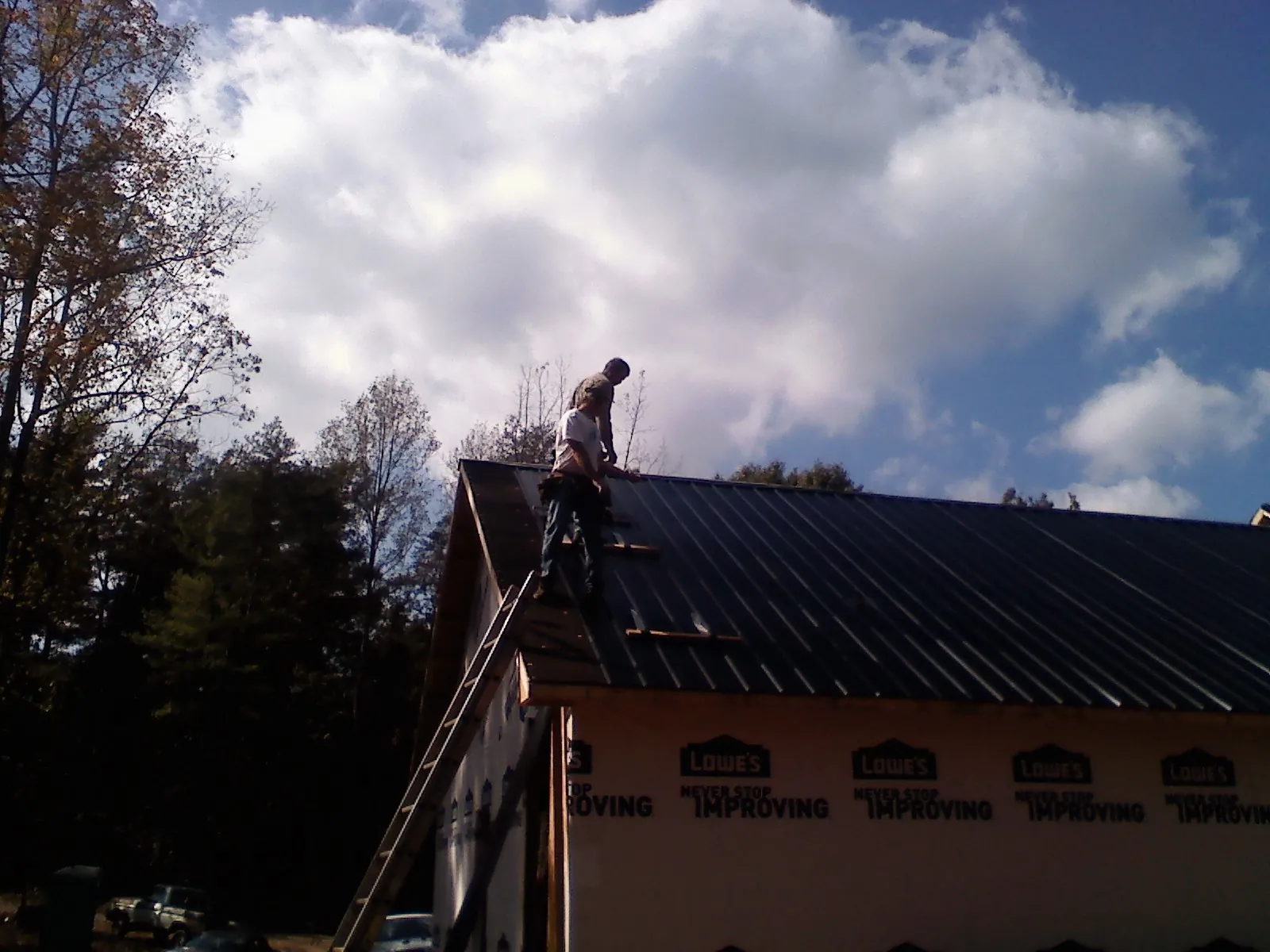 Roofer fastening dark metal panels high against a cloudy sky, from a Roof Inspection job in Elderton