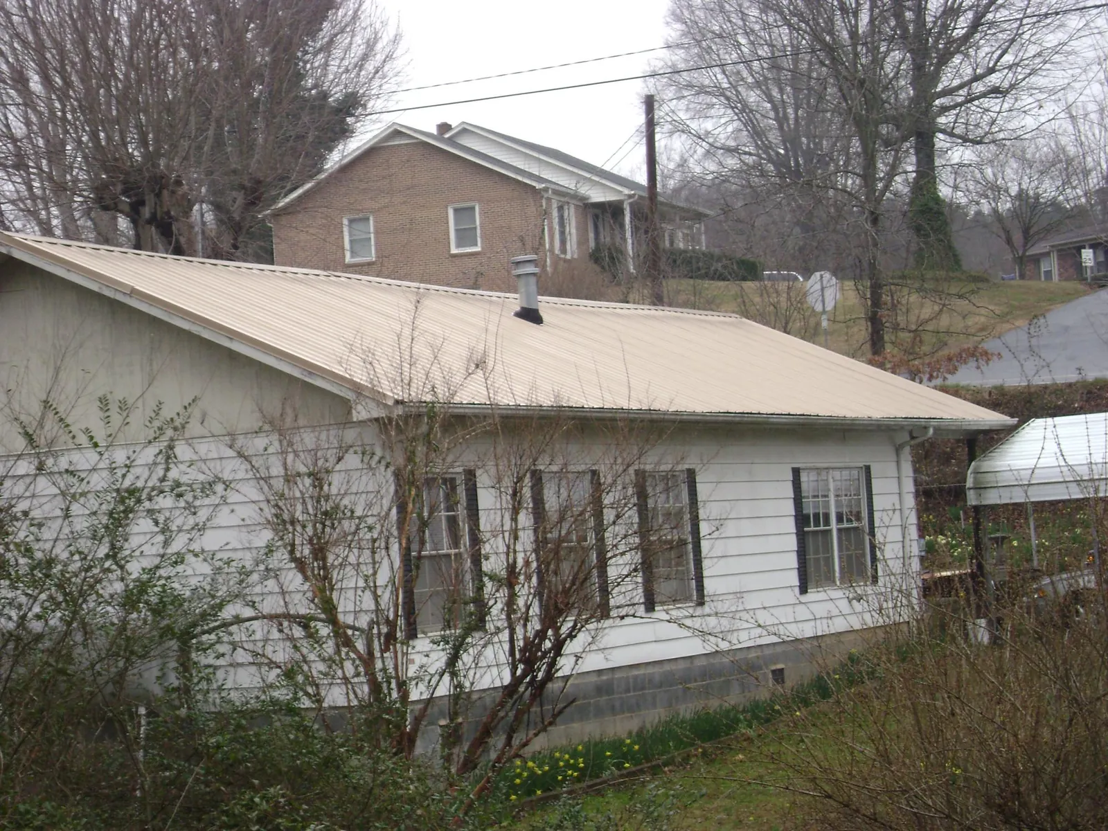 Tan metal roof on a white sided house set into a hillside — Commercial Roofing by Roofing Brothers in Elderton